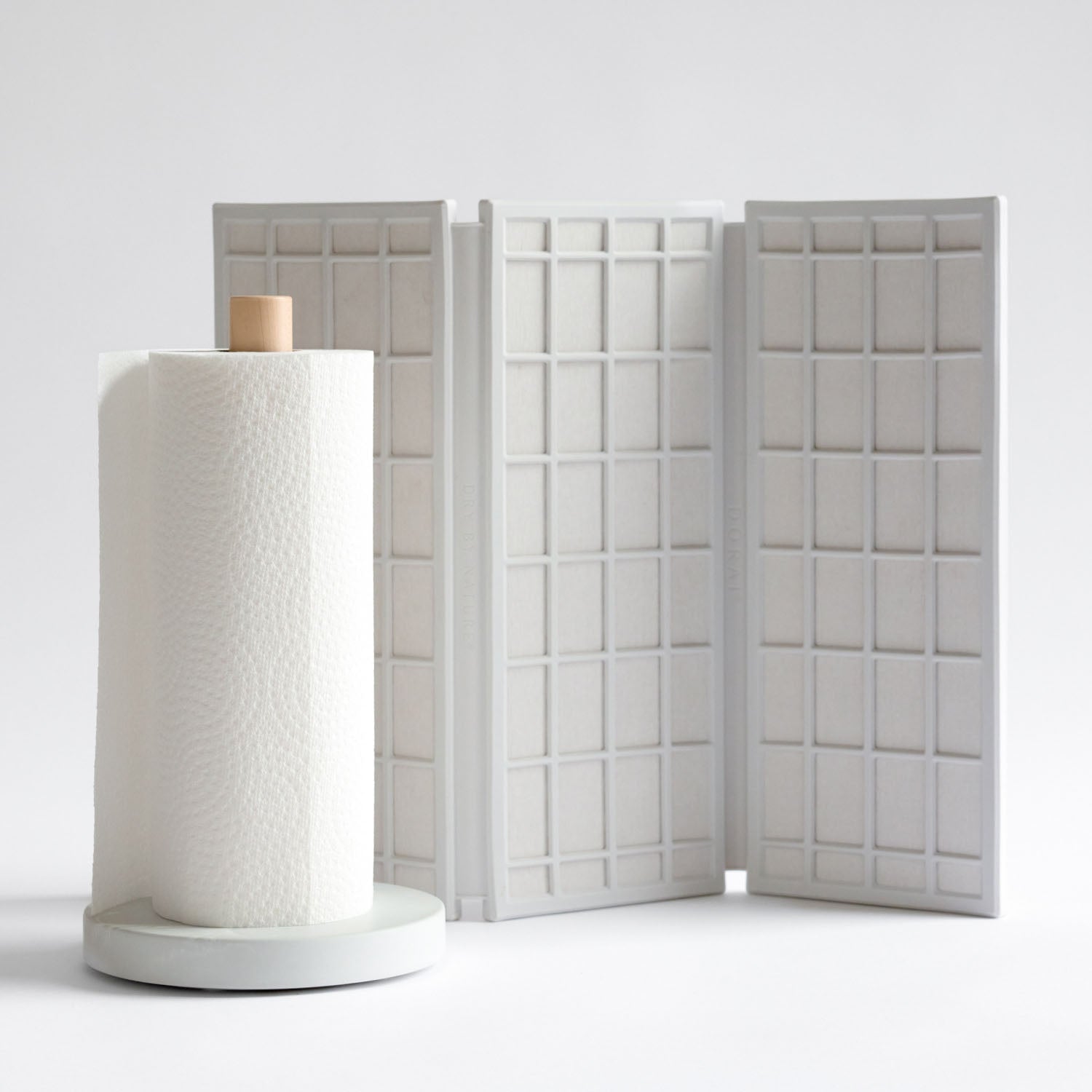 White paper towel holder with a roll of paper towels on a light gray background with dish mat