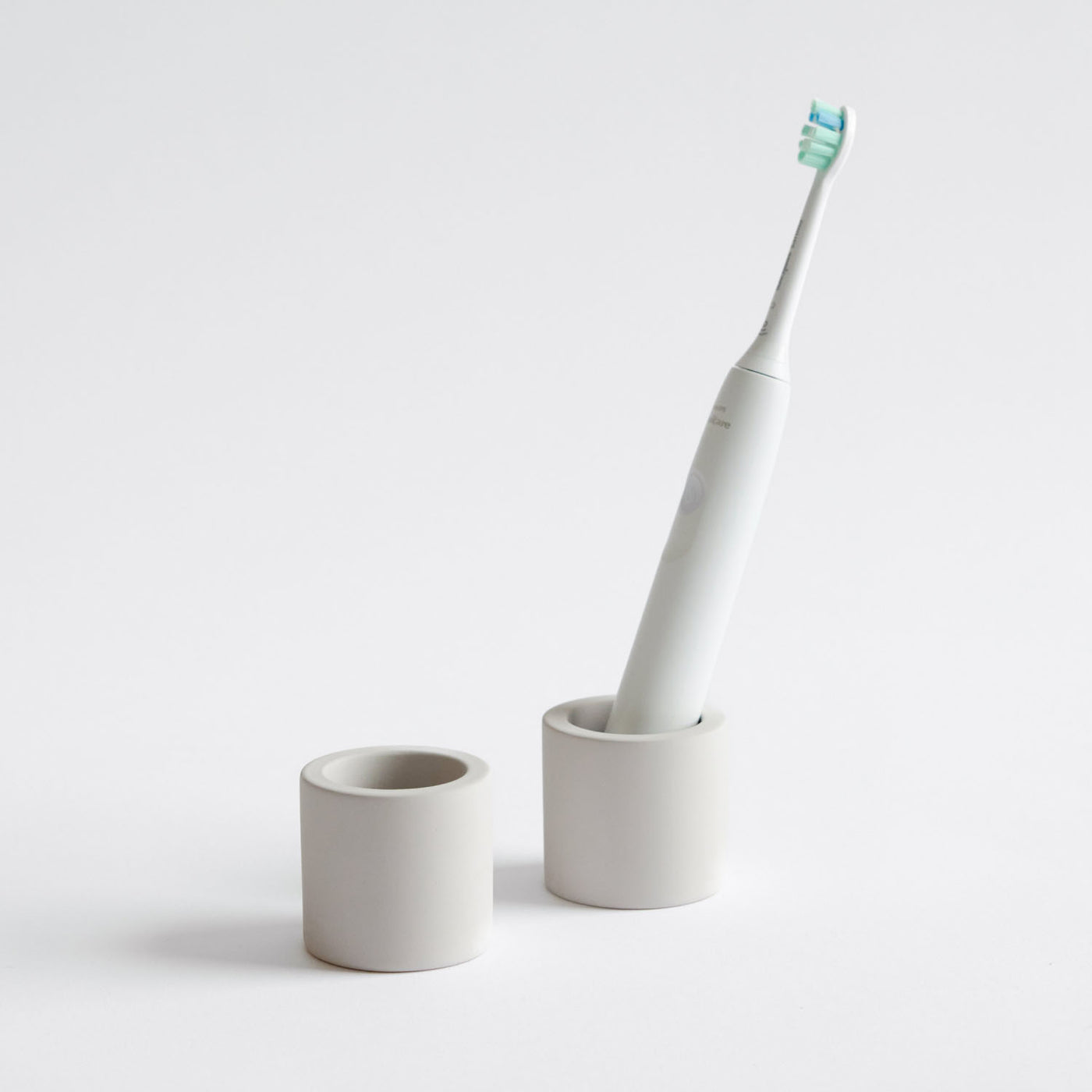Two stone toothbrush holders, one with an electric toothbrush inside on a white background