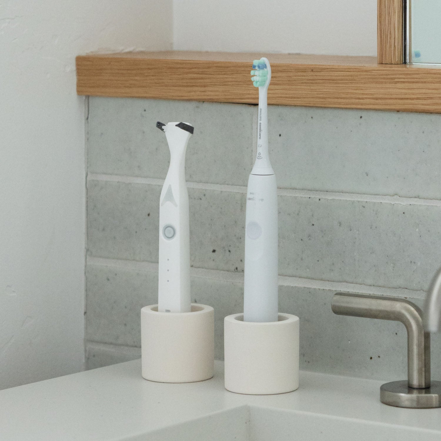 Two stone toothbrush holders, one holding an electric toothbrush and one holding an electric flosser, on a bathroom counter