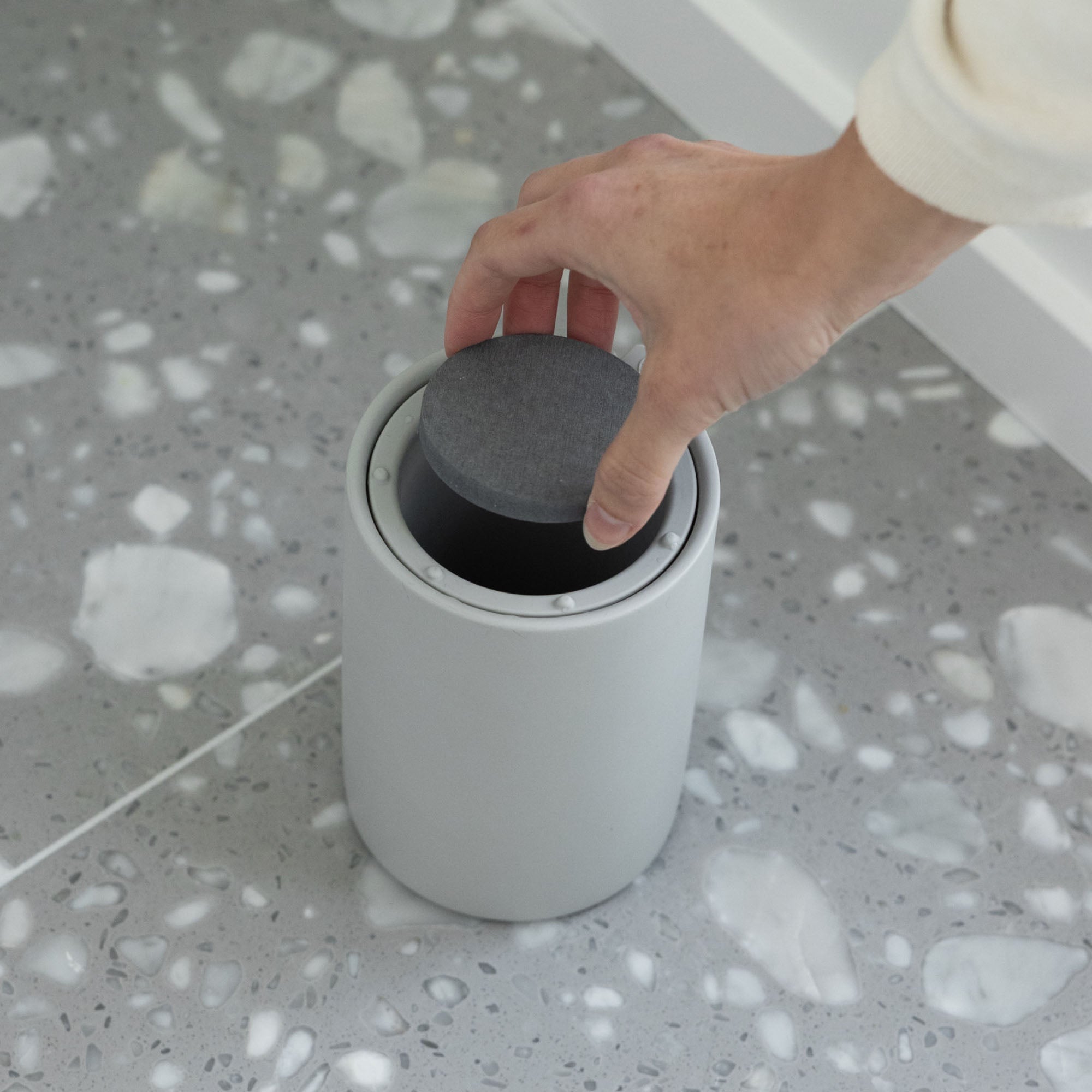 Hand placing moisture-absorbing stone in modern toilet brush holder.