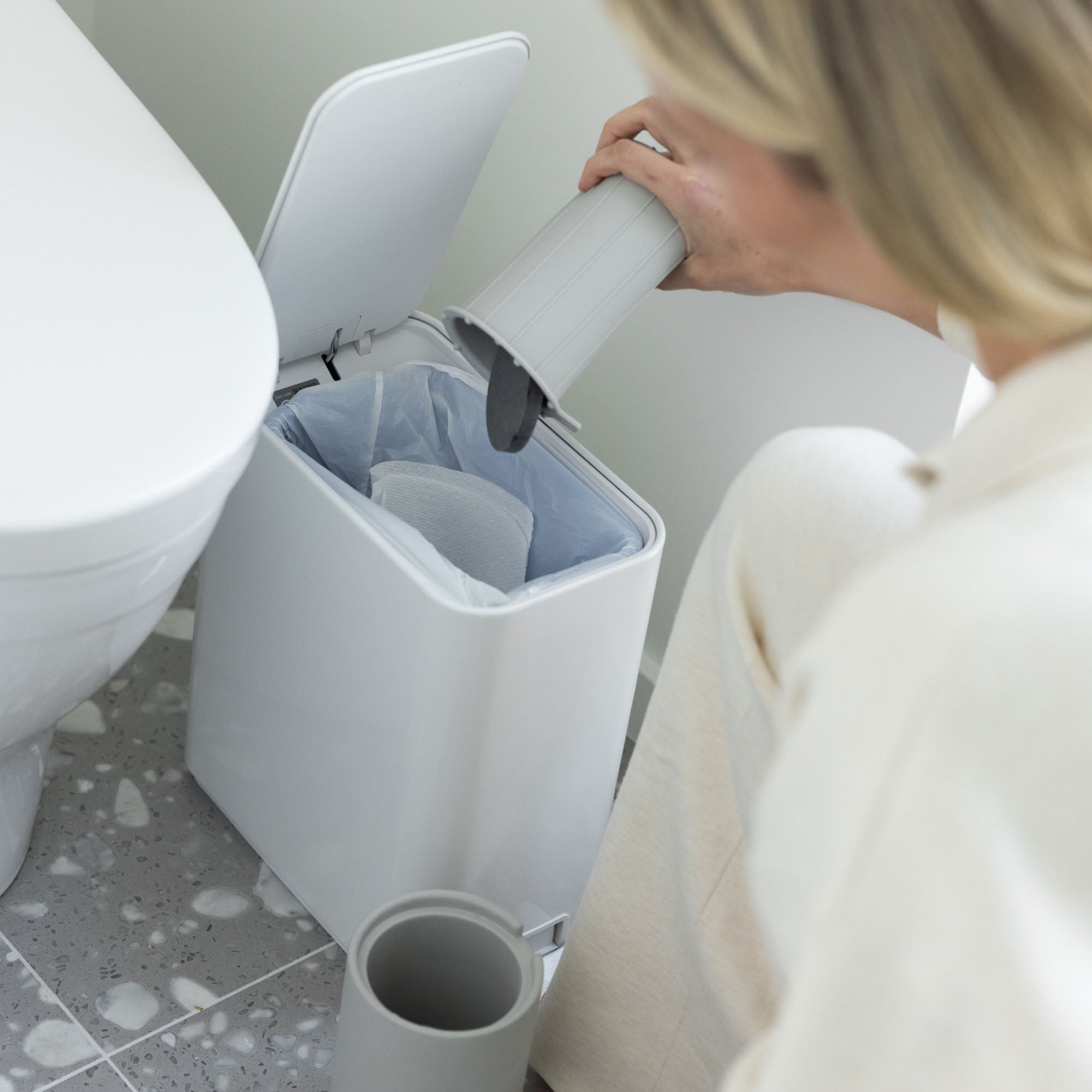 Person throwing away moisture-absorbing stone for modern toilet brush holder.