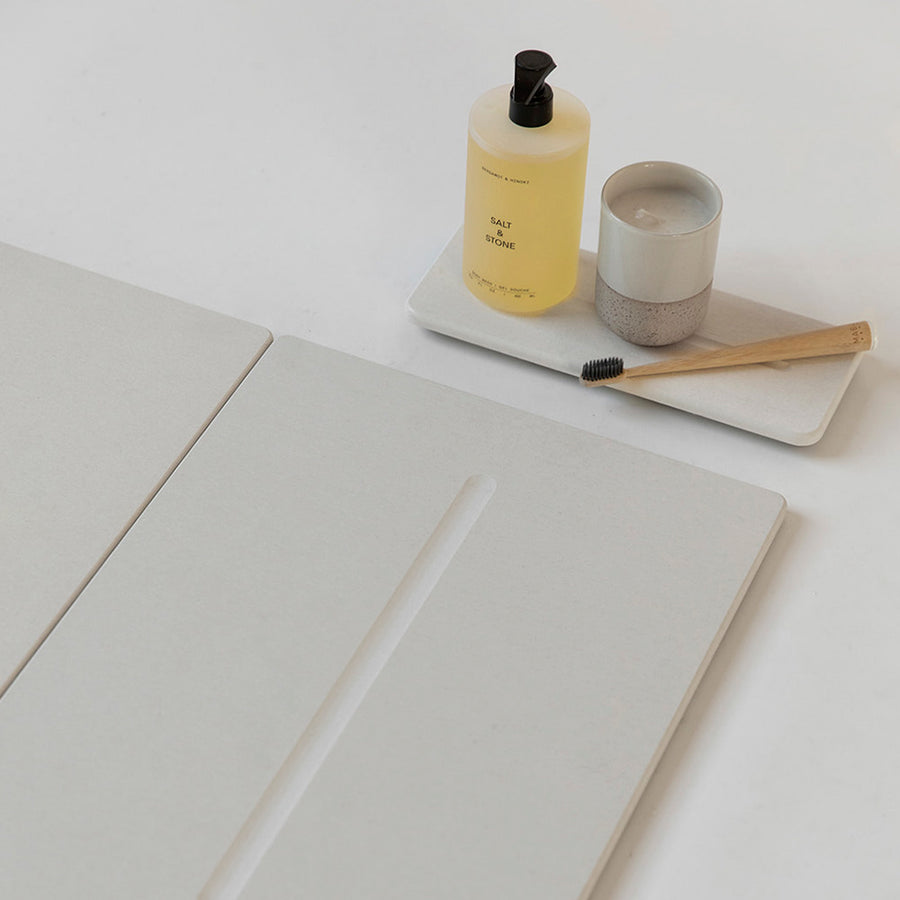 Sandstone, off-white sink organizer with brush and candle with matching Sandstone bathroom stone mat.